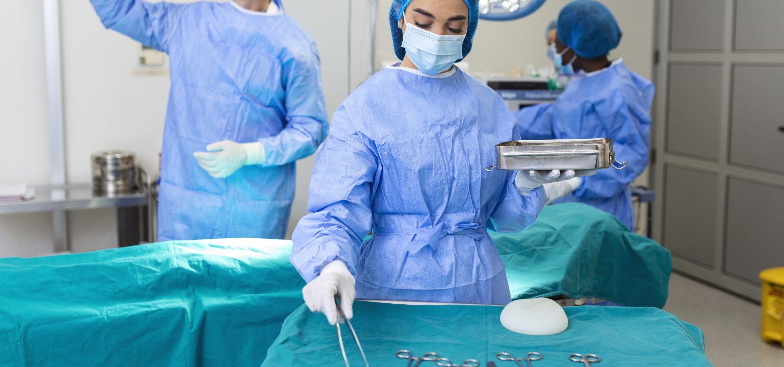 Female surgeon in surgical uniform taking surgical instruments at operating room. Young woman doctor in hospital operation theater