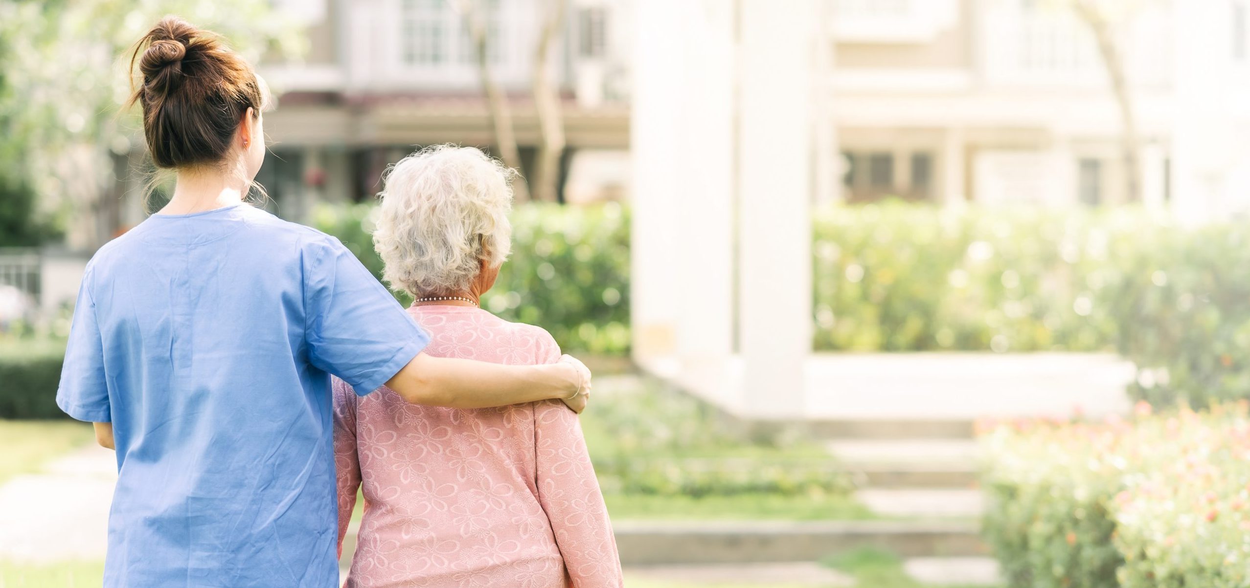 Back view of nurse caregiver support walking with elderly woman outdoor